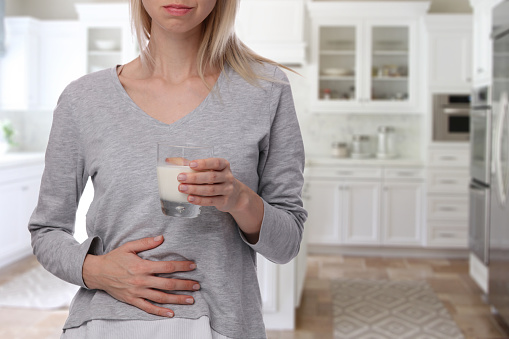 Dairy Intolerant person.Woman with stomach pain holding a glass of milk. Lactose intolerance, health care concept.