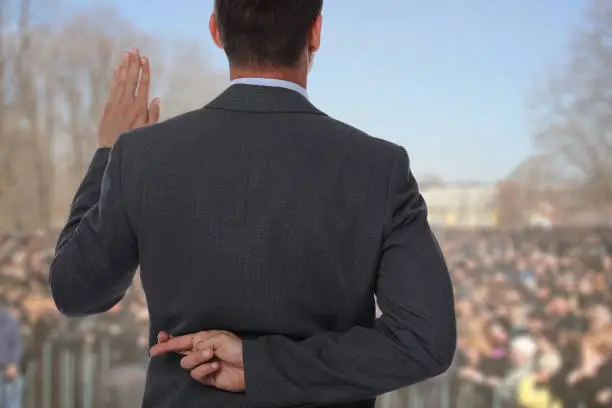 Photo of Politician liar gives people impossible promises with fingers crossed on his back.