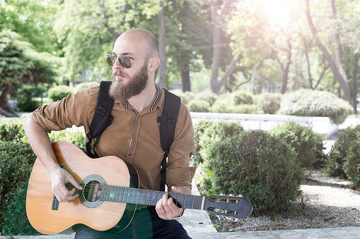 Man with a beard playing an acoustic guitar in a park