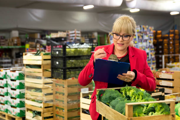 All as on list Young blond woman with eyeglasses, wearing a red jacket checking broccoli in a wooden crate at a fruit and vegetable warehouse in Slovenia, Europe. Piles of crates in the background. inspector stock pictures, royalty-free photos & images