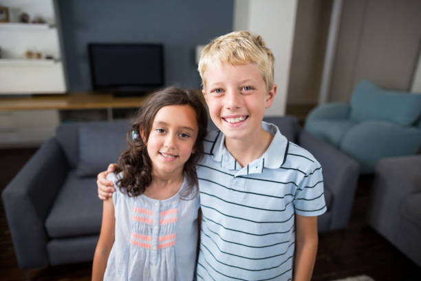 istock Siblings standing with arm around in living room 678439970