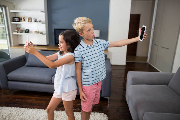 istock Siblings taking selfie on their mobile phone in living room 678443046
