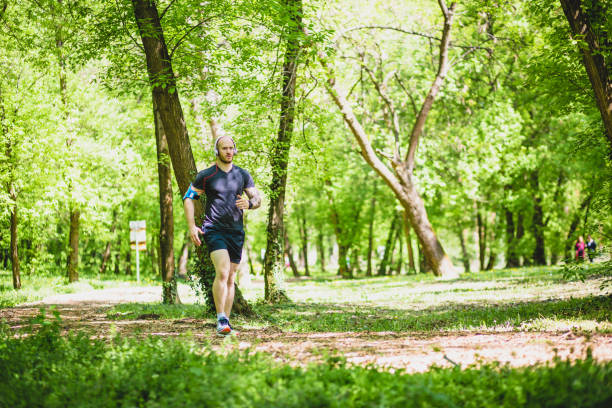 istock Young man with tatoo running in the park along beautiful trees. 678449130