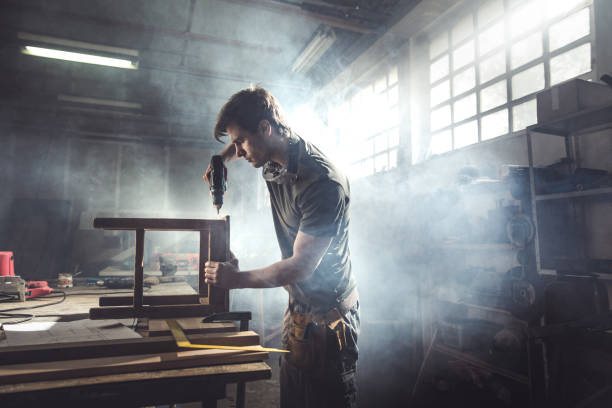 Male carpenter using drill to repair a chair in a workshop.