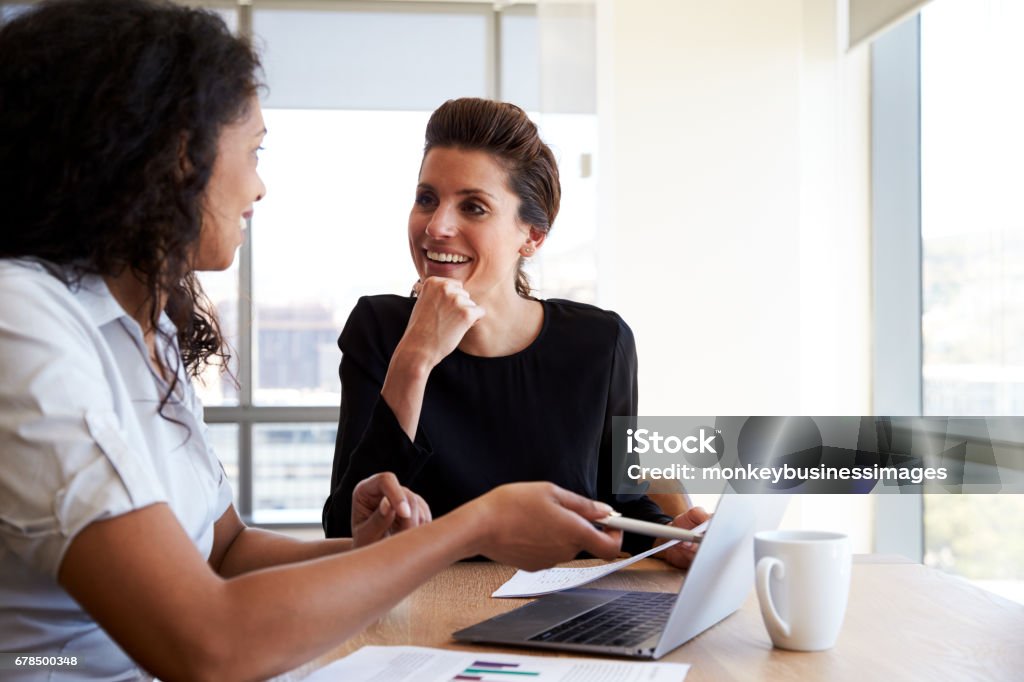 Duas mulheres de negócios usando o computador portátil numa reunião de gabinete - Foto de stock de Reunião de negócios royalty-free