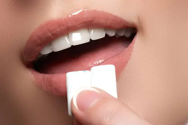 Closeup detail of woman putting pink chewing gum into her mouth. Chewing Gum, Eating, Women. Close up on a beautiful girl while enjoying a candy.