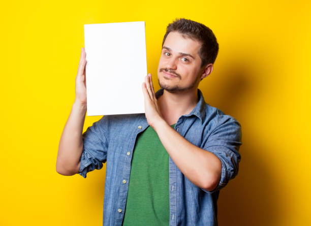 istock handsome young man holding white poster on the wonderful blue background 678508964