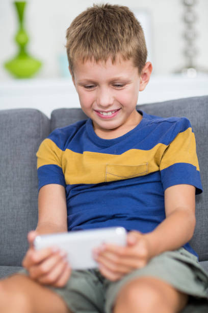 istock Happy boy sitting on sofa and using mobile phone in living room 678509288