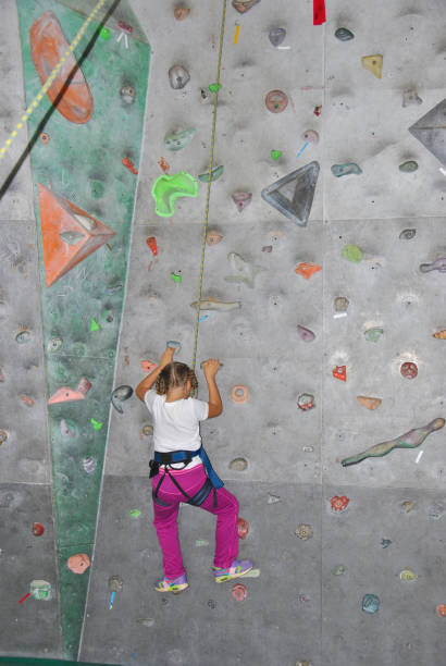 istock Infant girl in safety harness learning rock climbing doing first steps on vertical wall 678531190