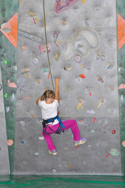 istock Infant girl in safety harness learning rock climbing doing first steps on vertical wall 678531198