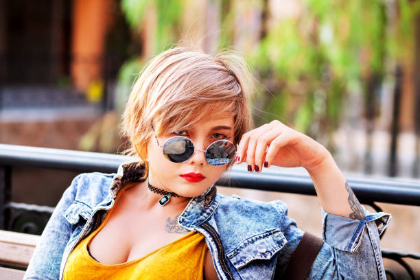 Thai woman in jeans jacket and with sunglasses sitting on a bench in sunshine in Bangkok
