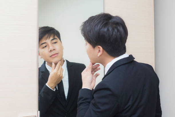 istock Young asian businessman doing up his tie knot in a mirror. 678553382