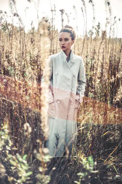 Outdoor fashion photo of young beautiful lady gray coat in autumn landscape with dry flowers