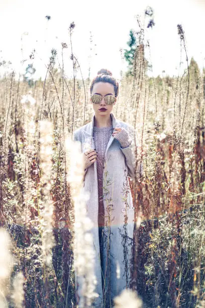 Outdoor fashion photo of young beautiful lady gray coat in autumn landscape with dry flowers