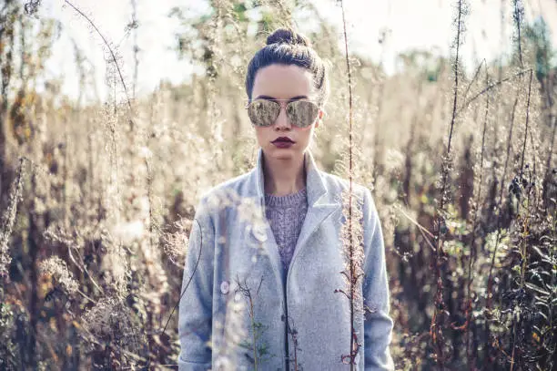 Outdoor fashion photo of young beautiful lady gray coat in autumn landscape with dry flowers