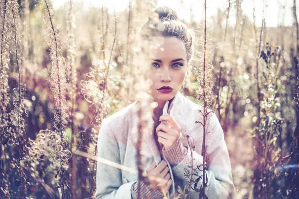 Outdoor fashion photo of young beautiful lady gray coat in autumn landscape with dry flowers