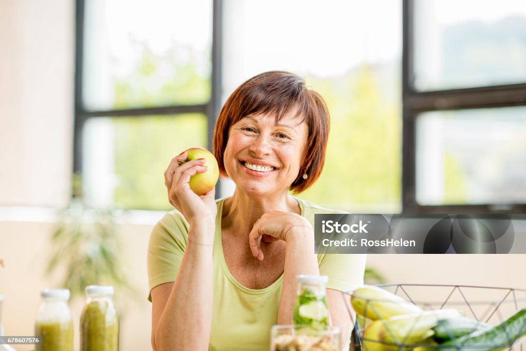 Older woman with healthy food indoors Portrait of a beautiful older woman with green healthy food on the table indoors on the window background Eating Stock Photo