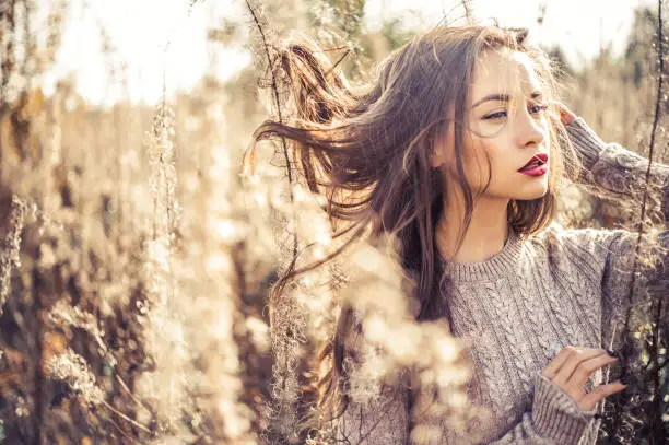 Outdoor fashion photo of young beautiful lady in autumn landscape with dry flowers. Knitted sweater, wine lipstick. Warm Autumn. Warm Spring