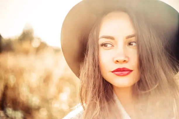 Outdoor fashion photo of young beautiful lady in autumn landscape with dry flowers. Gray coat, black hat, wine lipstick. Warm Autumn. Warm Spring