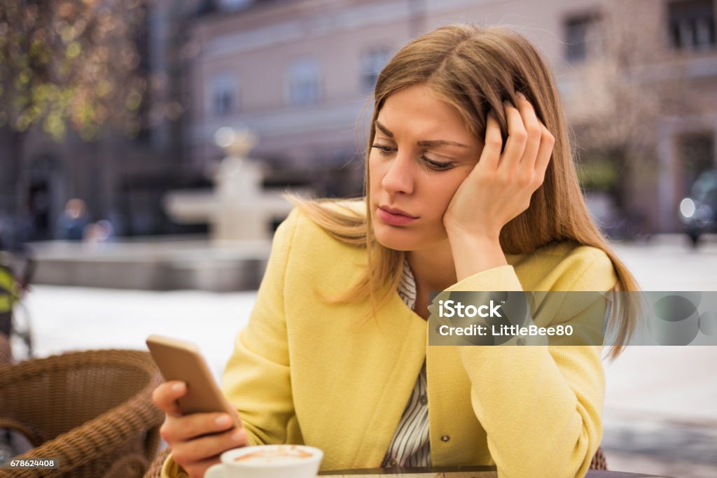Sad woman looking at her phone Lonely woman looking at her mobile phone while sitting at the cafe. Waiting Stock Photo