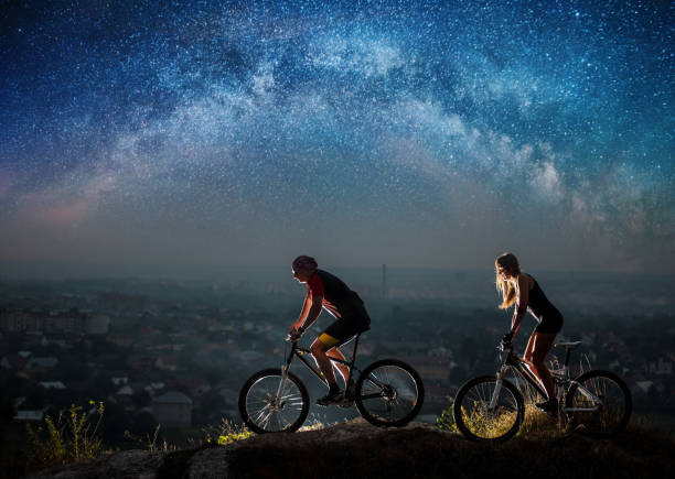 istock Sporty couple riding a bicycles at night under starry sky 678626928