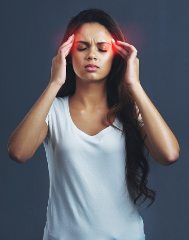 Studio shot of a young woman suffering with a headache highlighted in glowing red against a dark background