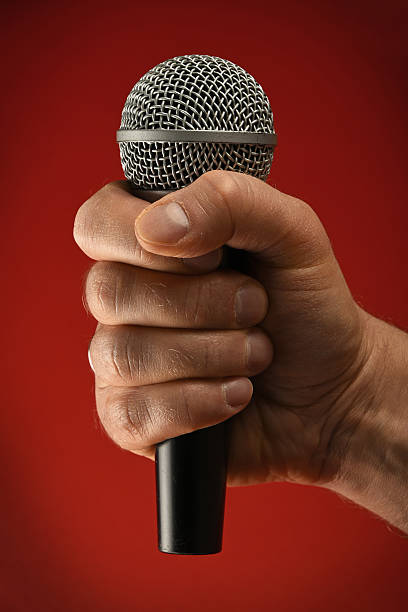 istock Cropped Hand Holding Microphone Against Red Background 678648447