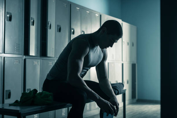 Man sitting on bench in locker room after workout in gym Young man sitting on bench in locker room after workout in gym locker room stock pictures, royalty-free photos & images