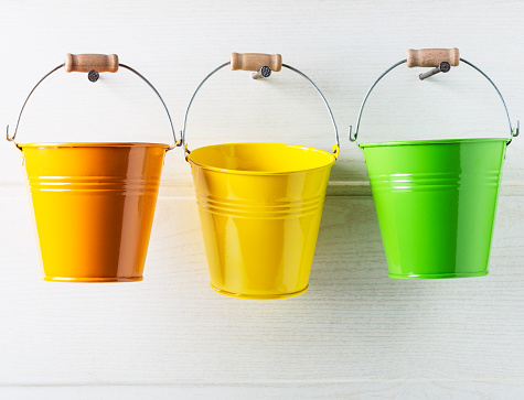 Bucket list concept. Three colorful buckets hanging on white wooden wall