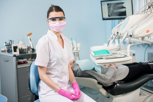 Retrato de joven mujer dentista con paciente en el consultorio dental. Médico de usar gafas, mascarilla, guantes blancos del uniforme y rosados. En el fondo de pantalla con la radiografía de los dientes del paciente. Odontología photo