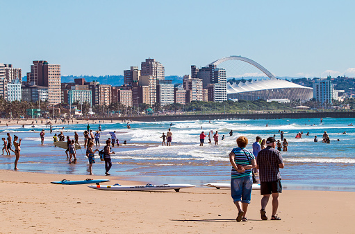 DURBAN, SOUTH AFRICA ; APRIL 24, 2017: Many unknown people on morning visit to beach against Durban city skyline and Moses Mabhida Stadium  in South Africa