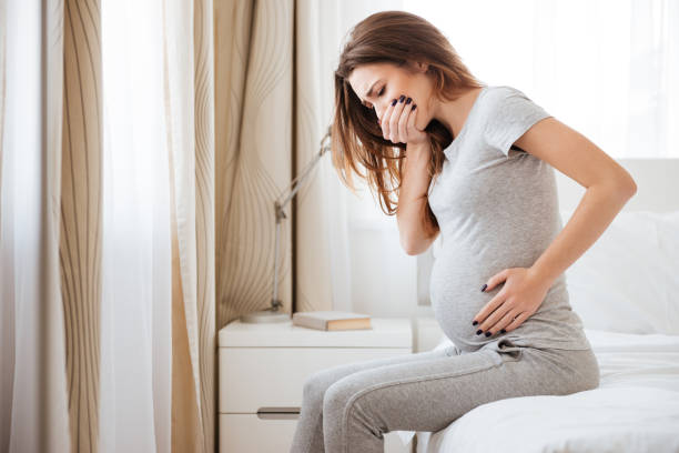 Pregnant young woman sitting on bed and feeling sick stock photo