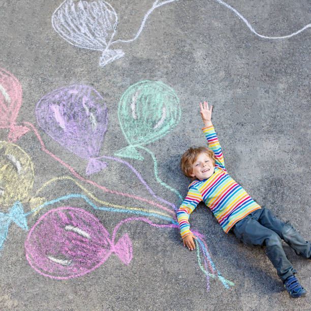 istock Kid boy having fun with colorful balloons drawing with chalks 678726706