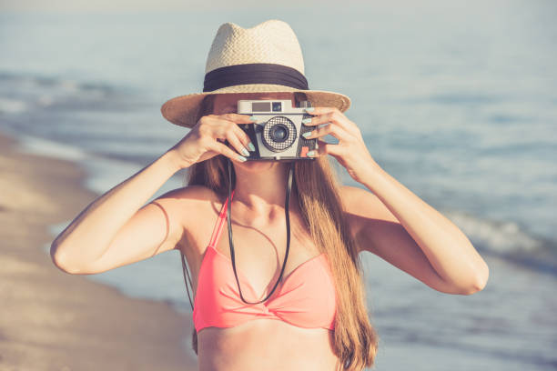 istock Young woman taking photo on the beach using retro camera 678729012