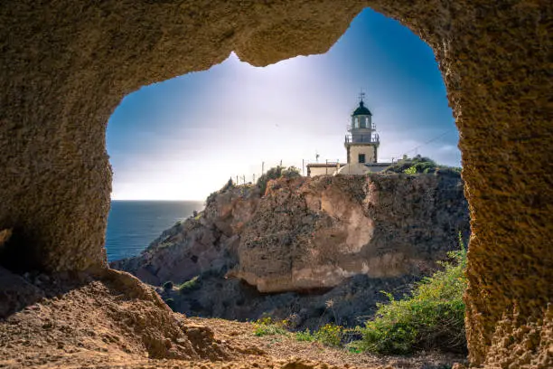 Photo of Lighthouse at Akrotiri through a frame of a window of a cave, Santorini, Greece.