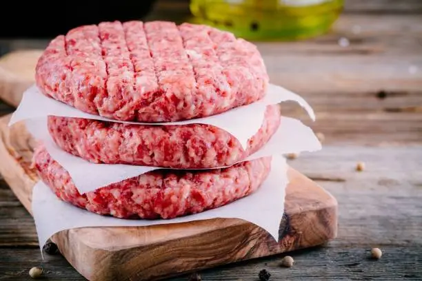 Ingredients for burgers: raw minced beef cutlets on wooden background