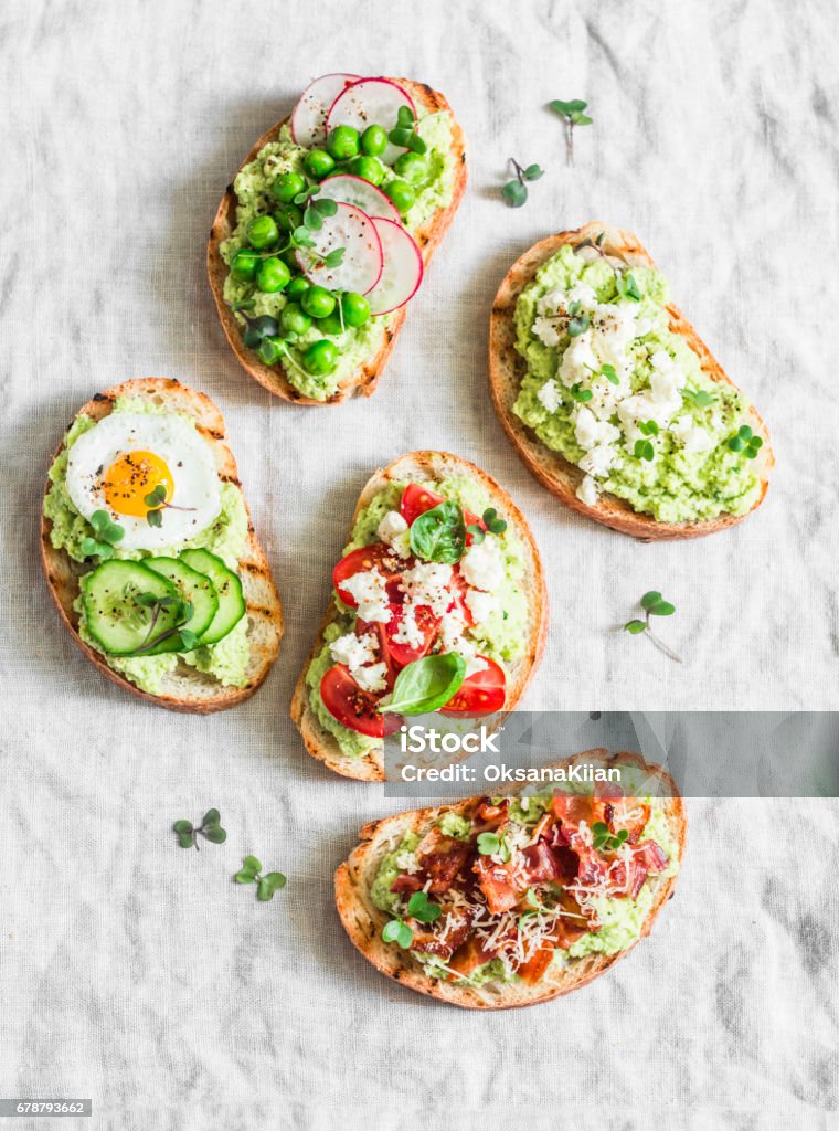 Variation avocado sandwich - with crispy bacon, quail egg, tomatoes, goat cheese, green peas, radish, cucumber. Healthy snack. On a light background, top view Avocado Stock Photo