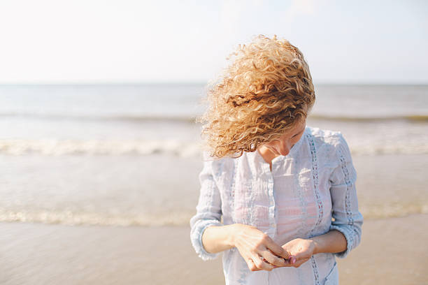 mujer joven recogiendo conchas marinas en la playa - sensory perception shell using senses women fotografías e imágenes de stock