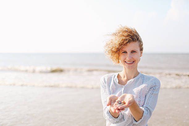 une femme tenant des coquillages sur sunny beach - sensory perception shell using senses women photos et images de collection
