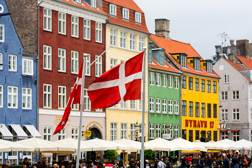 Danish Flags in front of colorful houses and resturants, street cafes at Nyhavn in Copenhagen - one of the most popular tourist places in Denmark. Nyhavn, Copenhagen,Denmark