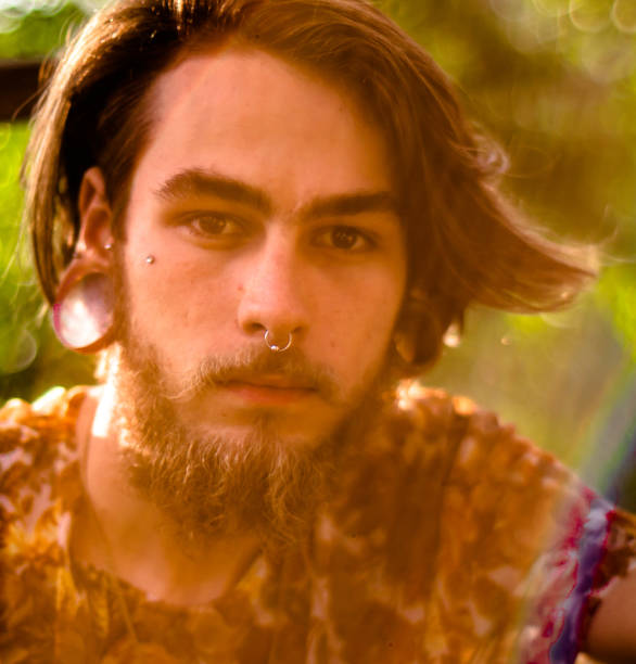 Face portrait of a young man with beard and brown hair, nose piercing and exotic earring photographed at dusk