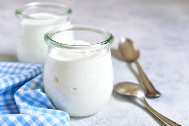 Two portions of fresh natural  homemade organic yogurt Two portions of fresh natural  homemade organic yogurt in a glass jar on a light slate background. yoghurt stock pictures, royalty-free photos & images