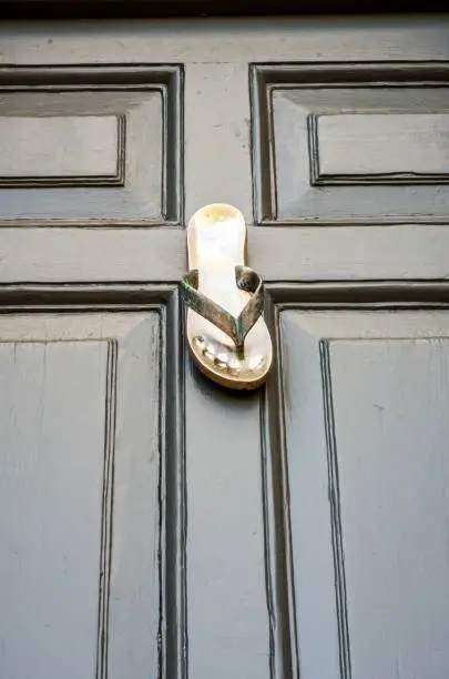 Photo of Brass knocker shaped flip-flops, beautiful ornament on brown wood, decorative entry element of the house