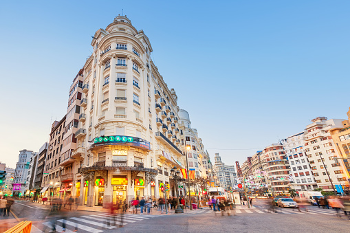 Wide angle stock photograph of pedestrians crossing street in downtown Valencia, Spain with ornate apartment houses in the backround