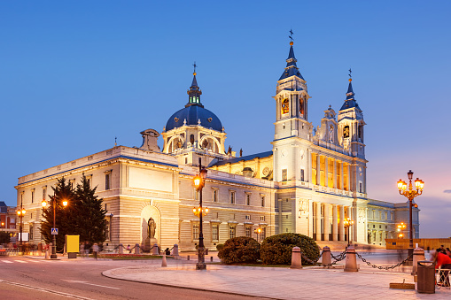Stock photograph of the landmark Almudena Cathedral aka Cathedral of Saint Mary the Royal of La Almudena (Santa Maria la Real de La Almudena) in downtown Madrid, Spain, illuminated at twilight blue hour.