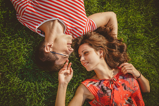 Young loving couple lying together head to head on a grass at summer. Family picnic. Both in red clothes and holding hands. Overhead top view.