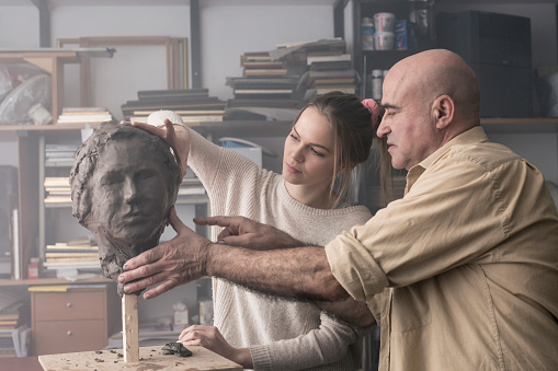 Teacher helping student sculpting clay face