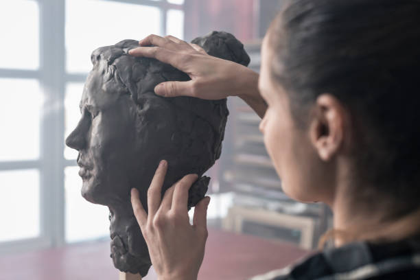 Young sculptor creates a clay sculpture Female artist sculpting face with clay in art studio clay sculpture stock pictures, royalty-free photos & images