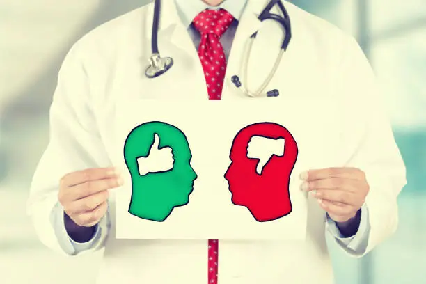 Closeup doctor hands holding white card with green red thumbs up thumbs down symbols inside signs shaped as human head isolated on hospital clinic office background. Retro instagram style filter image