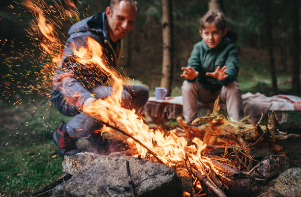 Father and son warms near campfire in forest Father and son warms near campfire in forest warms stock pictures, royalty-free photos & images